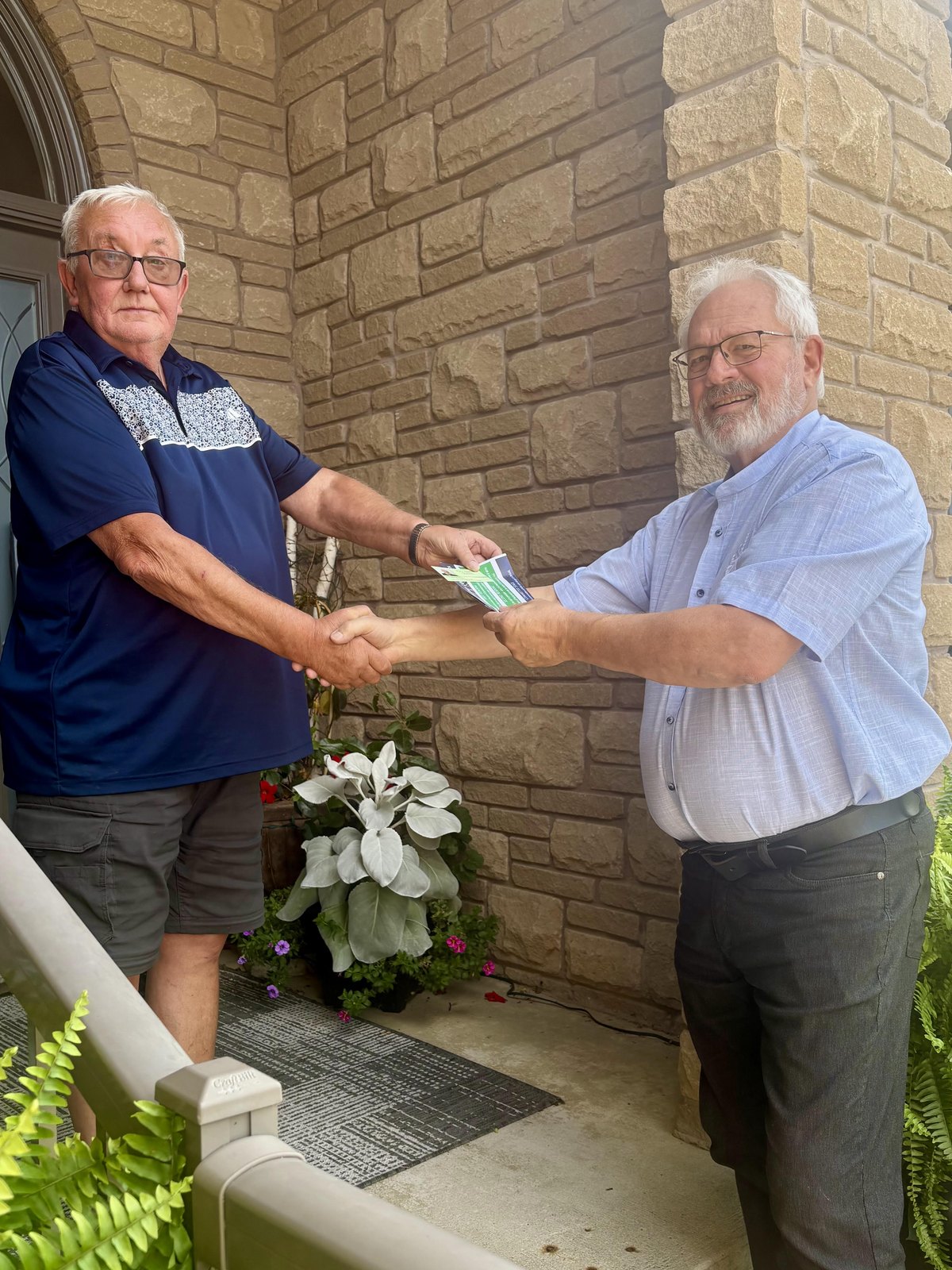 Tim Stanlick shaking hands with a resident at the front door, campaign literature in hand